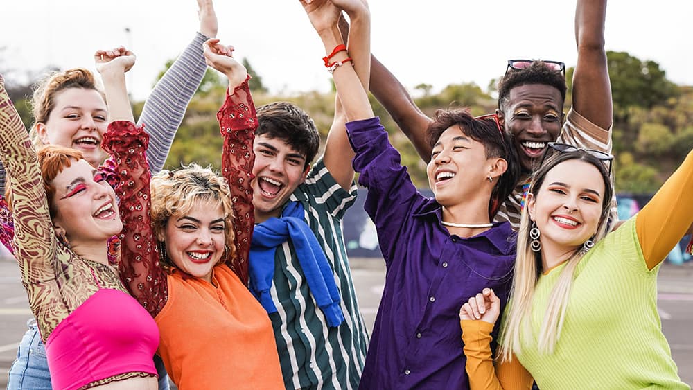 Multiracial LGBQ+ students having fun together sitting outside school.