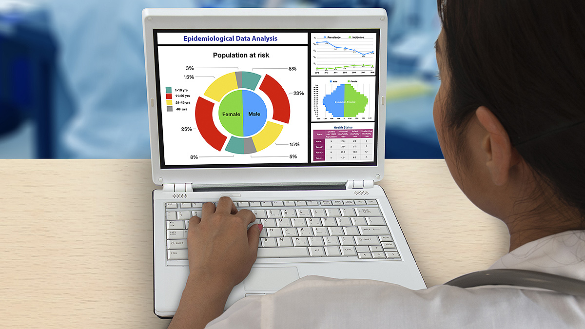 Scientist at computer with epidemiology data analysis charts and graphs on the screen.