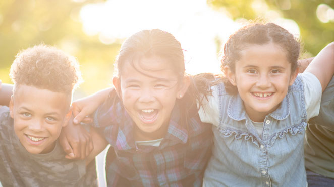 Three young children with arms around one another's shoulders.